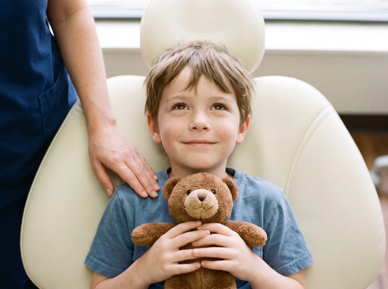 A child holding a teddy bear in the dental chair